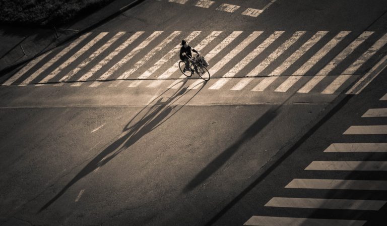 Black and white overhead photo of a cyclist crossing a zebra crossing in long shadows