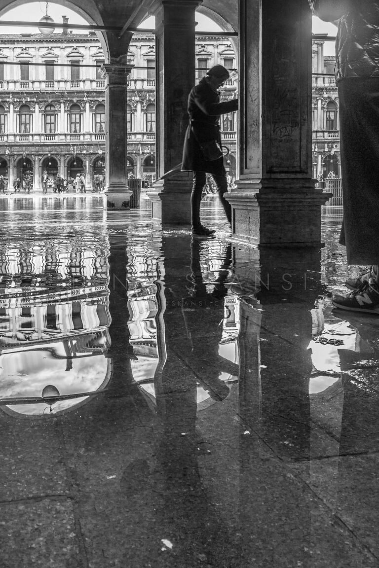 Black and white photo of arcade columns reflected in wet pavement