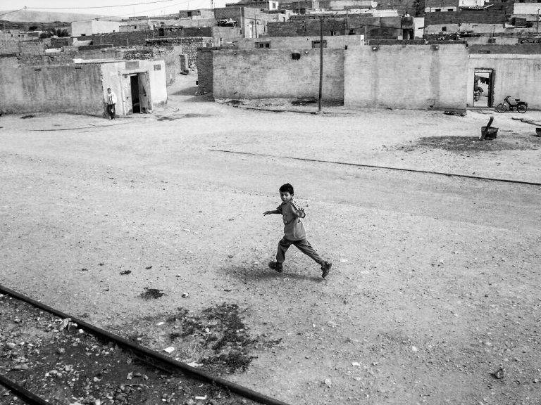 Black and white street photo of a child running across an empty square