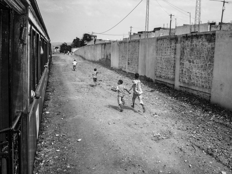 Black and white photo of children running along a dirt road beside a train