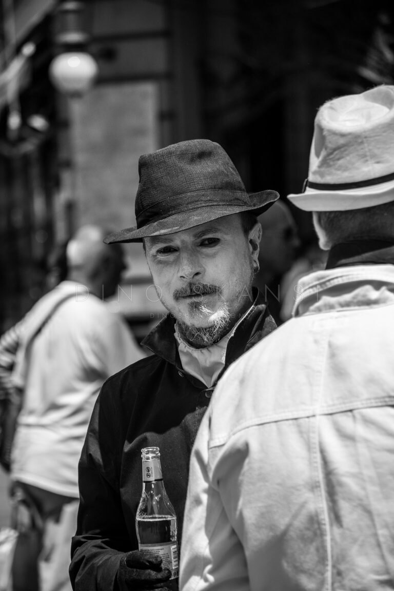 Black and white street photo of a bearded man in a hat among a crowd