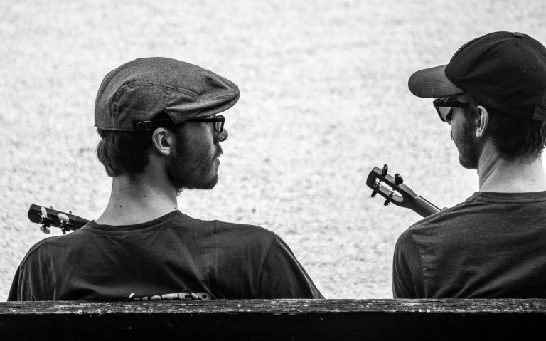 Black and white street photo of a man in a flat cap playing a string instrument