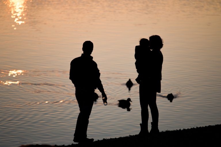 Silhouettes of an adult and a child at the water's edge at sunset