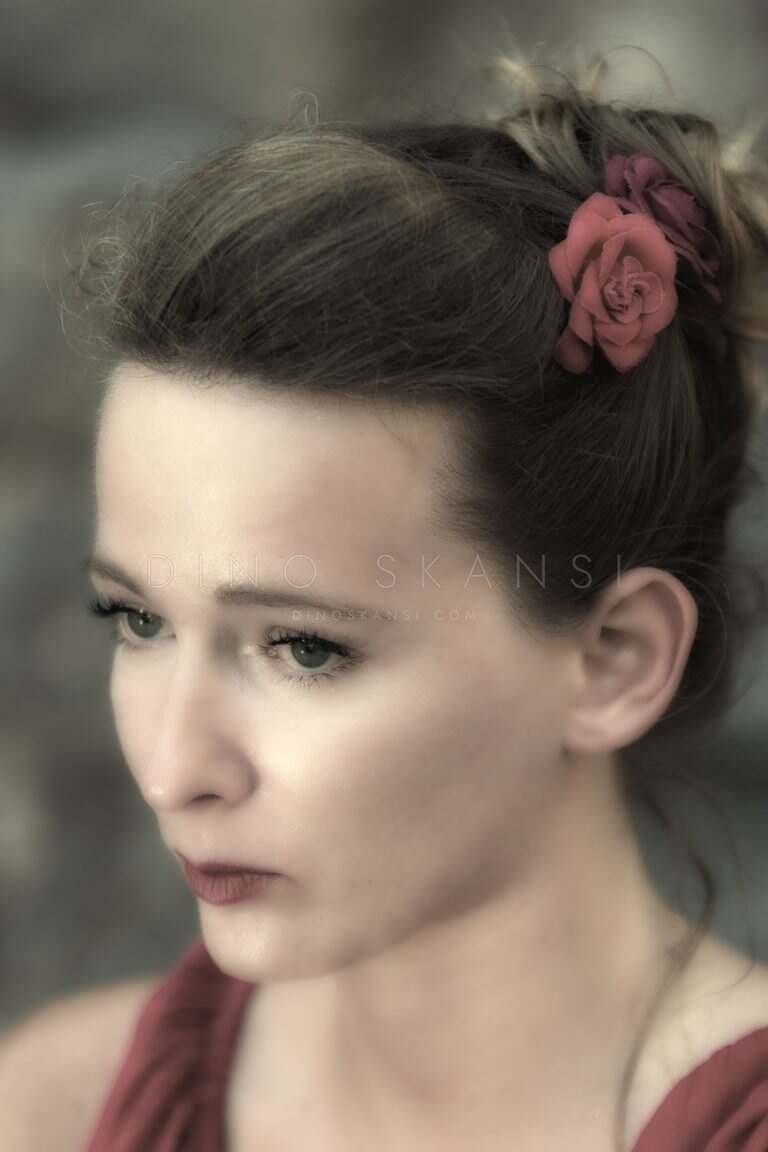 Colour portrait of a woman with a rose in her pinned-up hair, looking down
