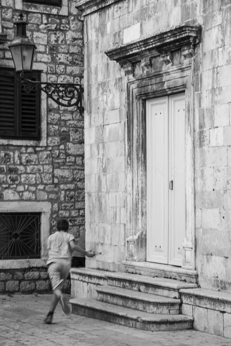 Black and white photo of a child standing in front of a large wooden door