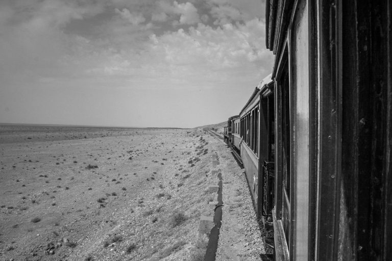 Black and white photo of a train passing through a flat open landscape
