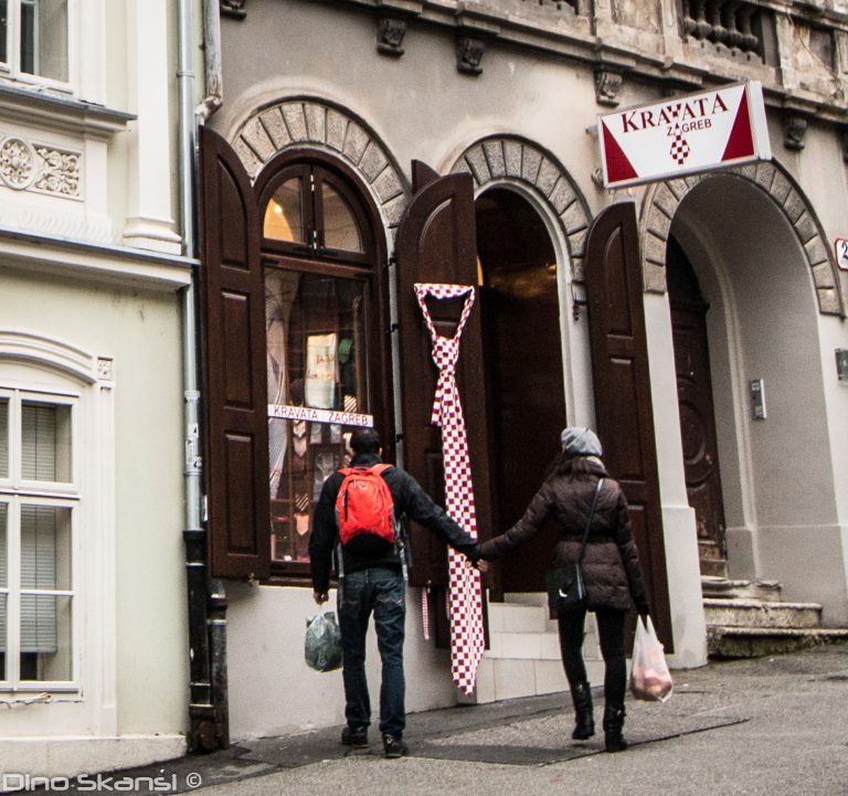 Colour street photo of two people walking past shopfronts with arched windows