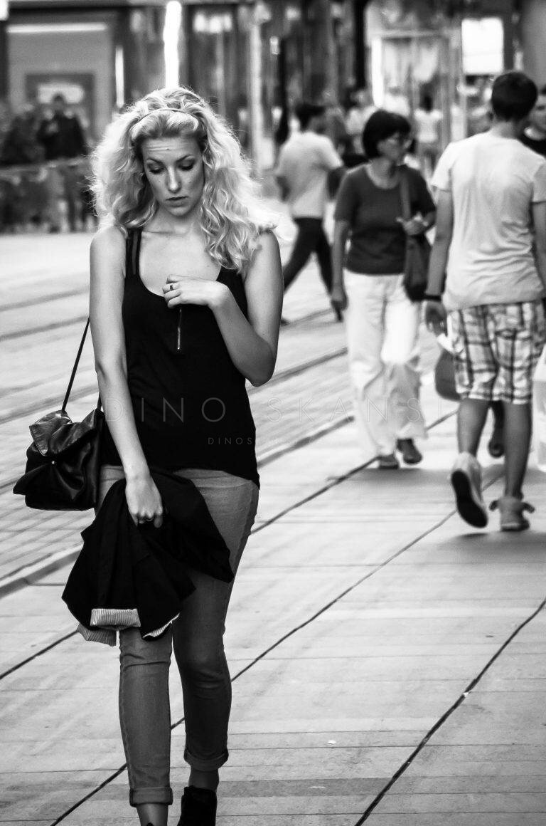 Black and white street photo of a woman in a black dress walking across a square