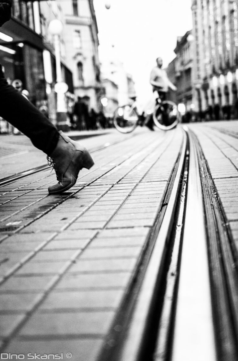 Black and white low-angle photo of tram tracks with a passer-by stepping into the frame
