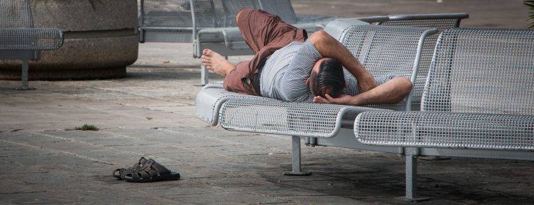 Colour street photo of a man sleeping on a metal bench