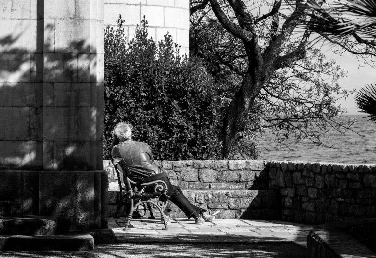 Black and white photo of a man sitting on a bench beneath a tree