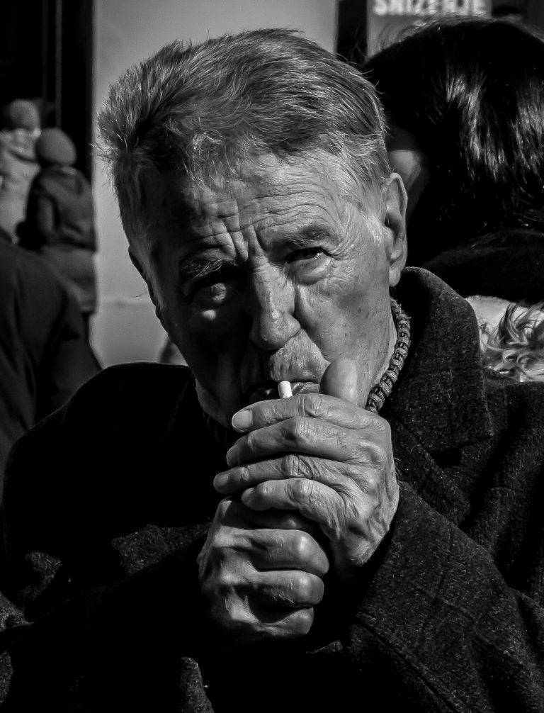 Black and white street portrait of an elderly man lighting a cigarette