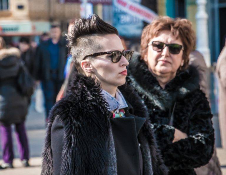 Colour street photo of two women in sunglasses and fur collars in a crowd
