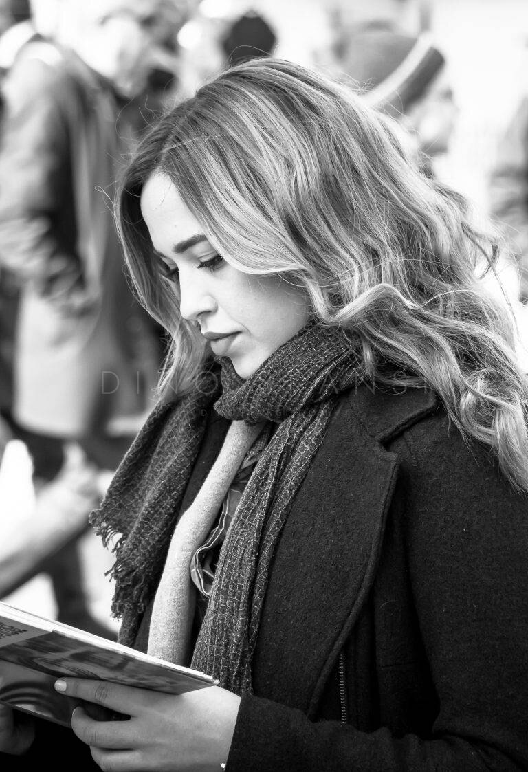 Black and white street portrait of a woman with long wavy hair and a scarf, looking down