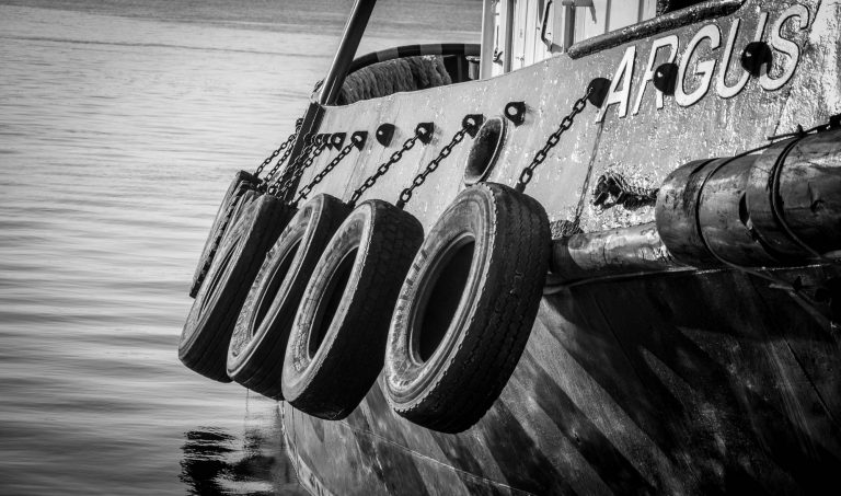Black and white close-up of old tyres hanging as fenders on a boat hull