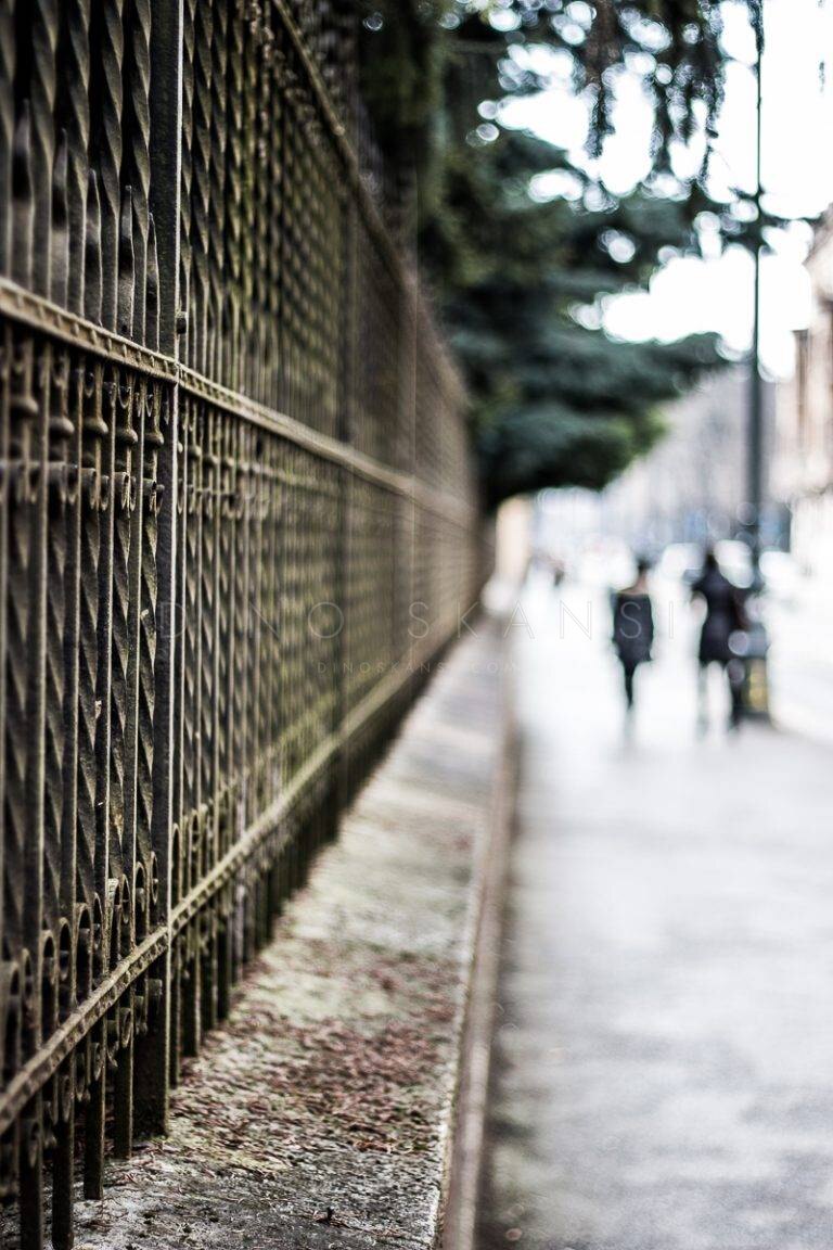 Iron fence in perspective along a pavement with pedestrians in the distance