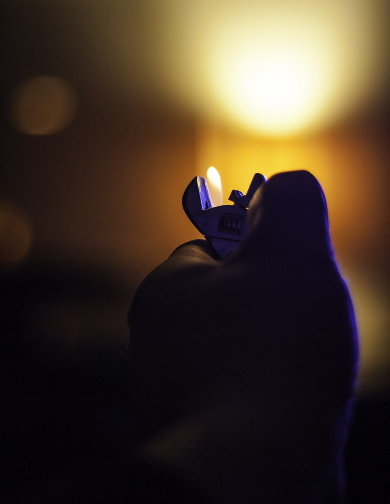 Dark silhouette against a warm glowing light with a small flame