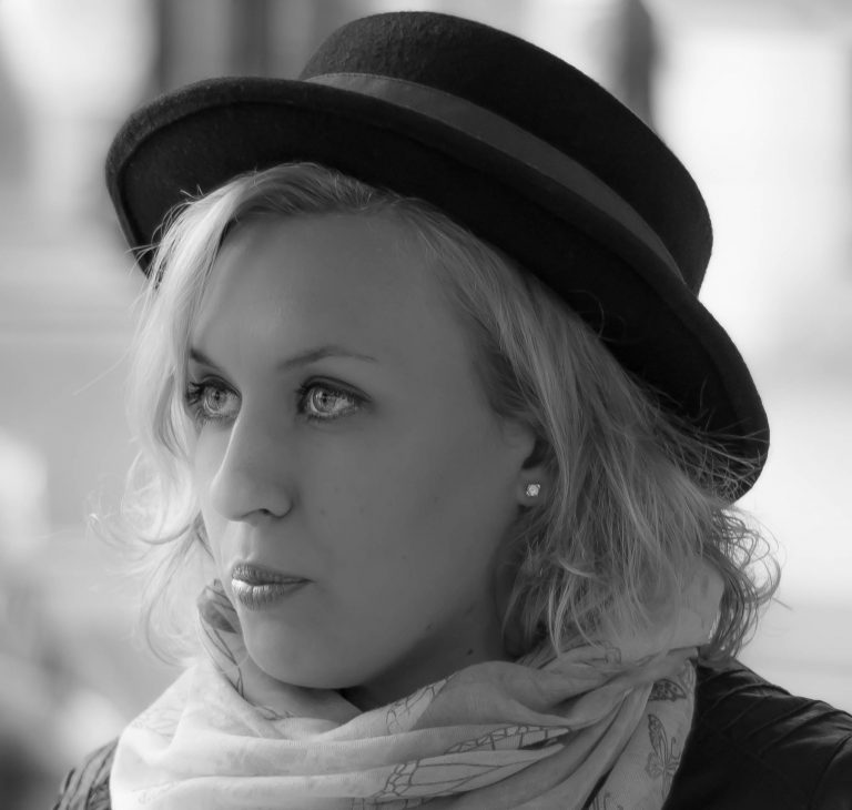 Black and white portrait of a woman in a bowler hat and scarf looking over her shoulder