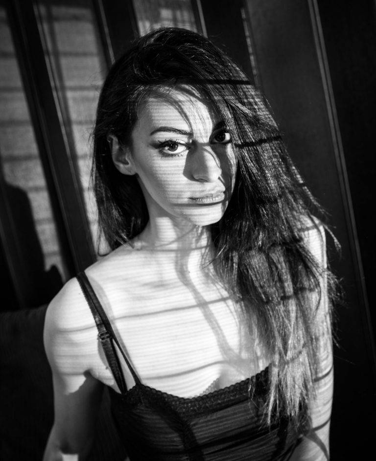 Black and white portrait of a woman with long dark hair in striped window light