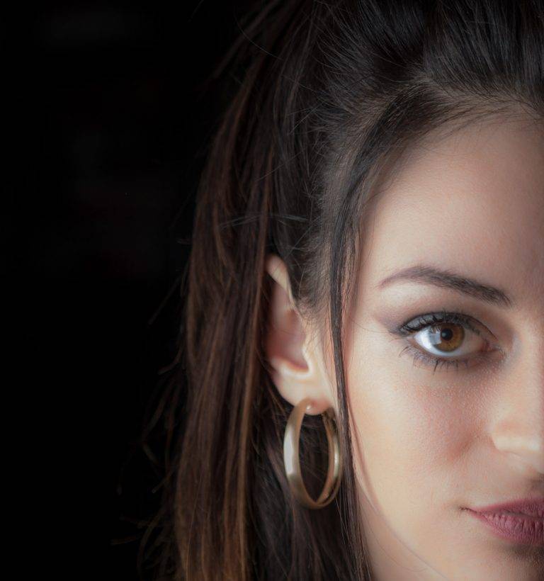 Colour half-face portrait of a woman with a hoop earring against a dark background