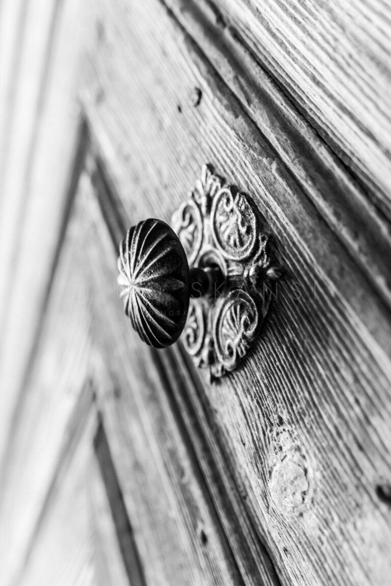 Black and white close-up of an ornate metal door knob on a wooden door