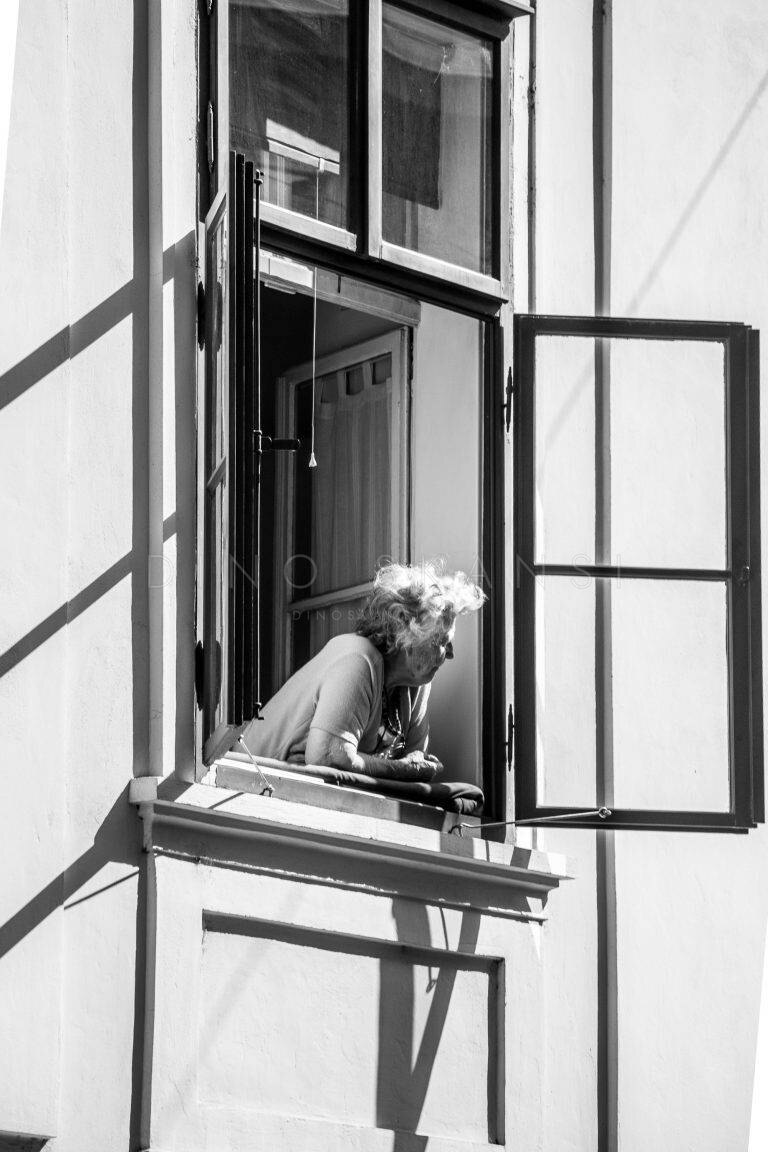 Black and white photo of an elderly woman leaning out of an open window