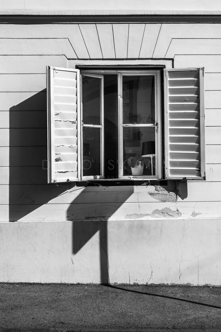 Black and white photo of an open window with wooden shutters casting a diagonal shadow