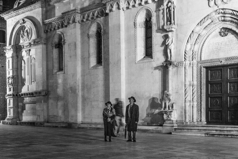 Black and white photo of two people walking past a church facade