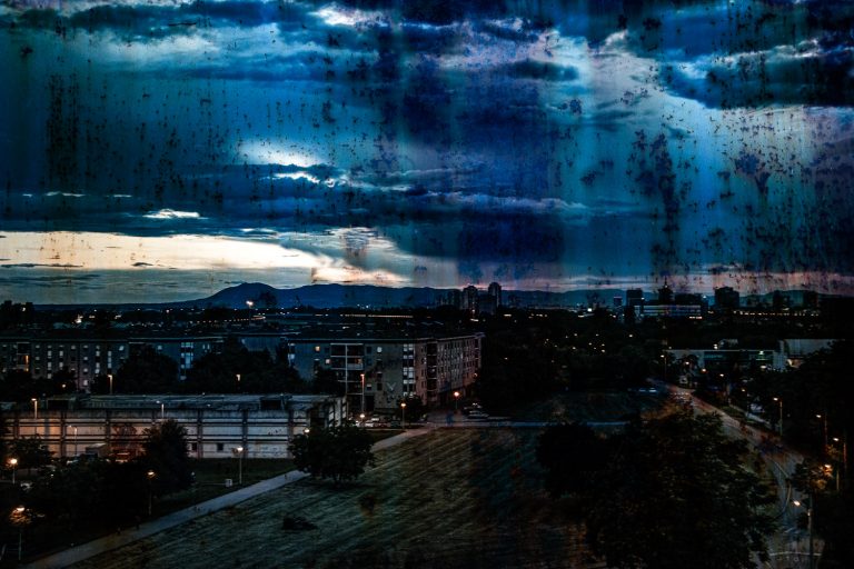 Blue-toned cityscape under dramatic storm clouds