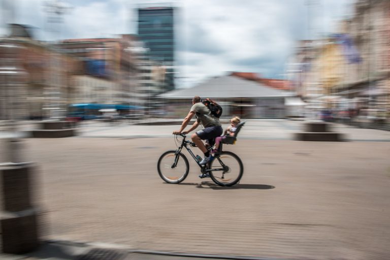 Panning street photo of a cyclist riding past a blurred city skyline