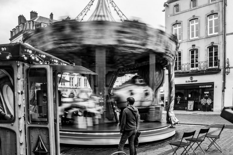 Black and white street photo of a child standing in front of a carousel in Metz, France