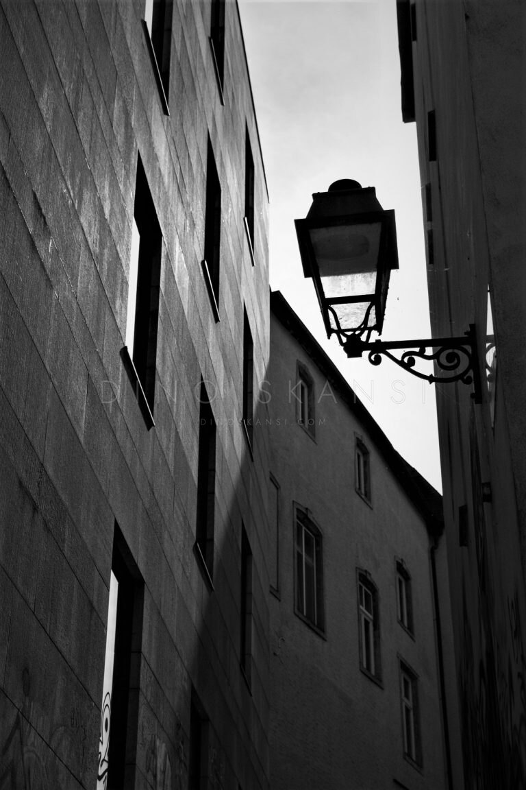 Black and white upward view of an old street lamp between buildings