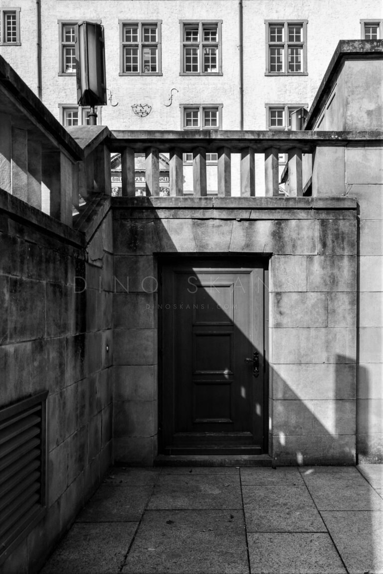 Black and white photo of a wooden door beneath a stone balcony