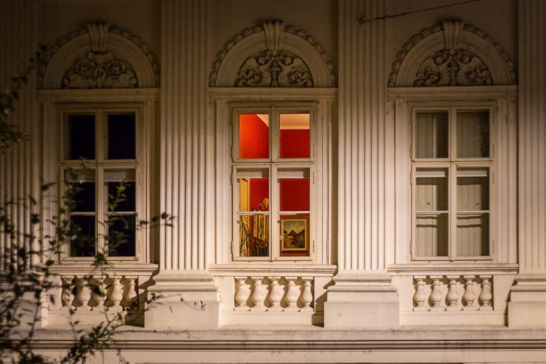 Building facade with ornate windows, one of them lit in red
