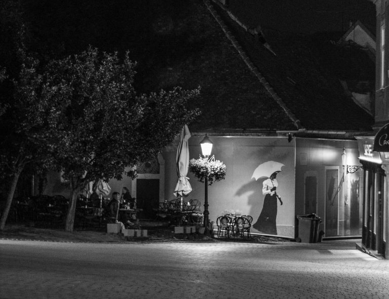 Black and white night scene with a street lamp and a figure under an umbrella
