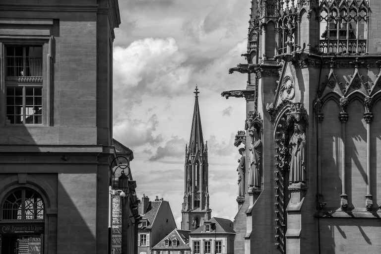 Black and white photo of a Gothic church spire seen between buildings