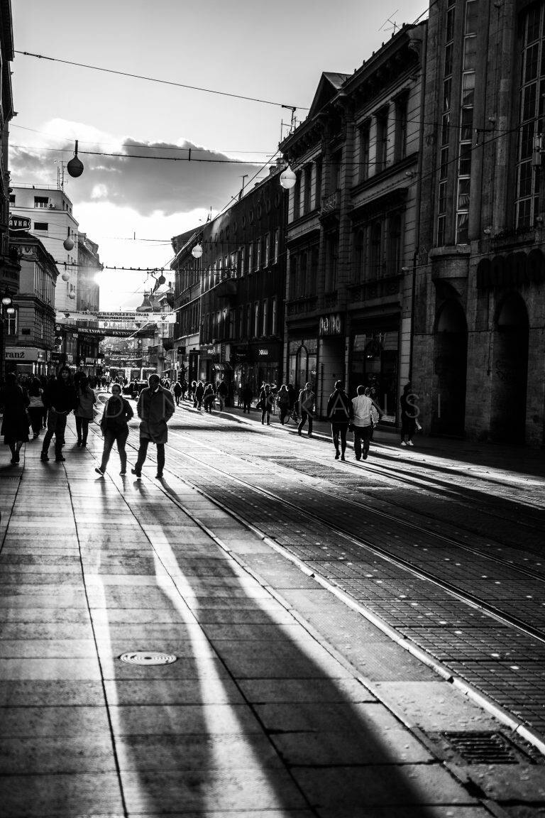 Black and white photo of a city street with tram tracks and pedestrians