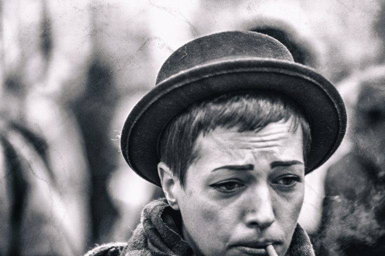 Black and white street portrait of a performer in a bowler hat with face paint