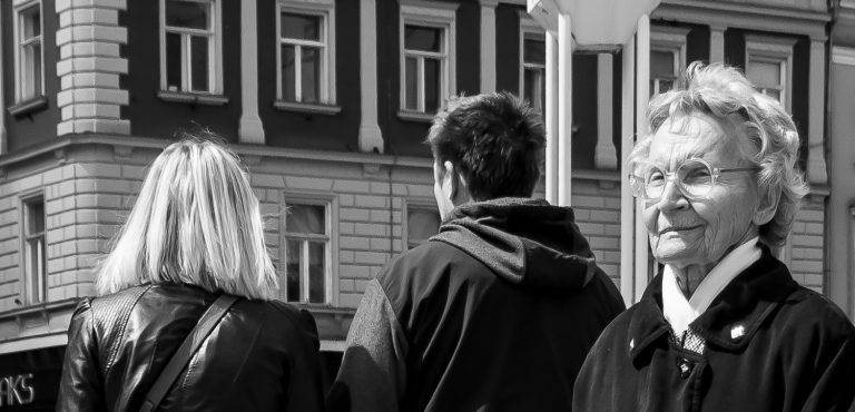 Black and white street photo of a young man in a hoodie seen from behind, facing a building
