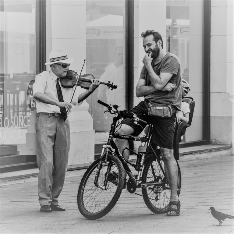 Black and white street photo of a violinist and a cyclist with his bicycle