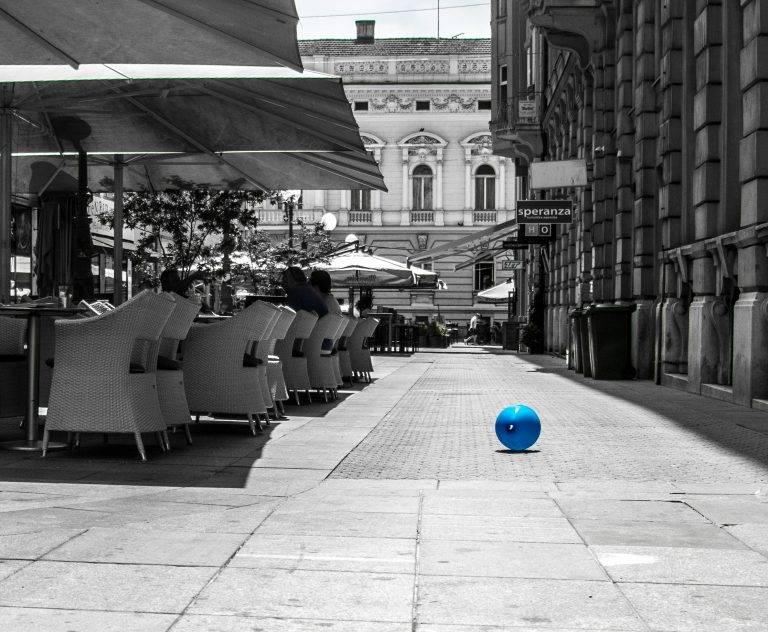 Black and white photo of a café terrace with a single blue ball on the pavement