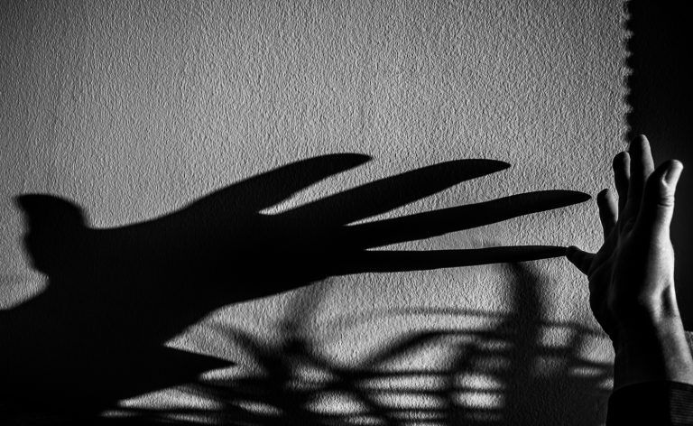 Black and white photo of the shadow of an outstretched hand on a textured wall