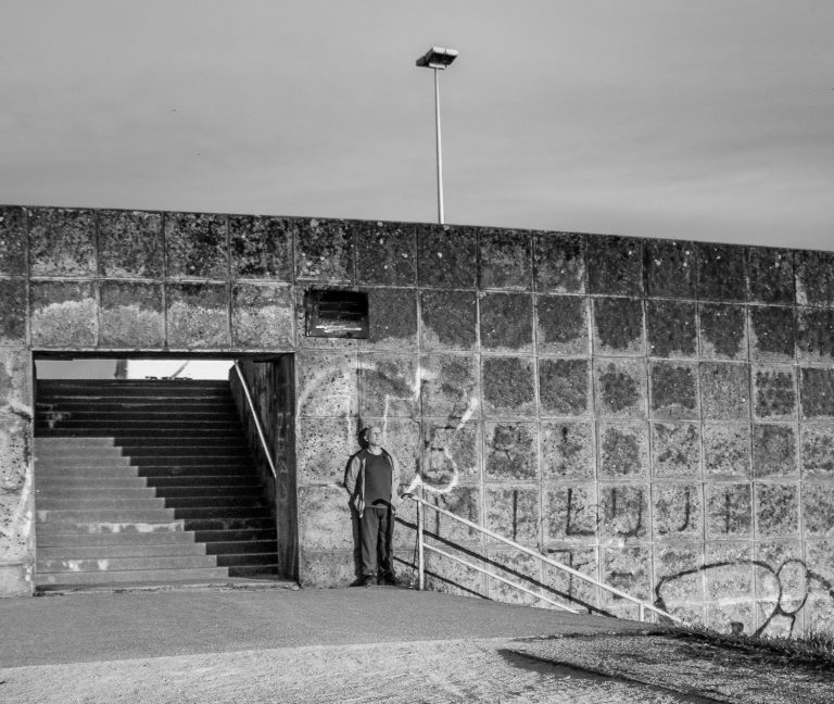 Black and white photo of a stone wall with a stairway entrance and a lone figure