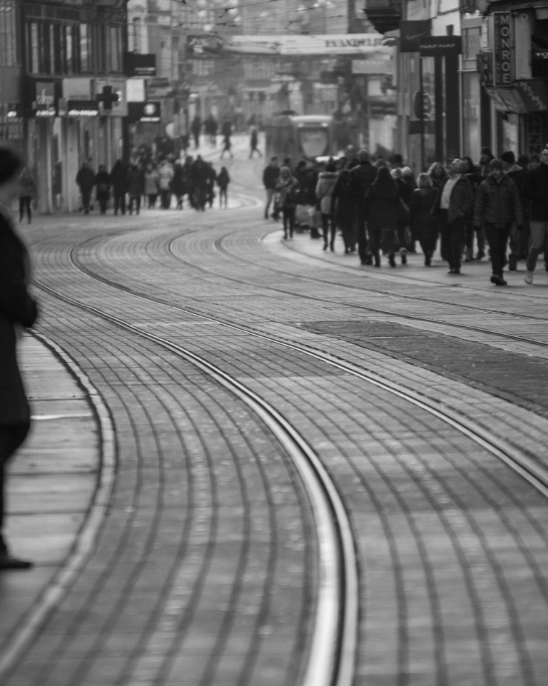Toned photo of tram tracks curving along a city street with pedestrians