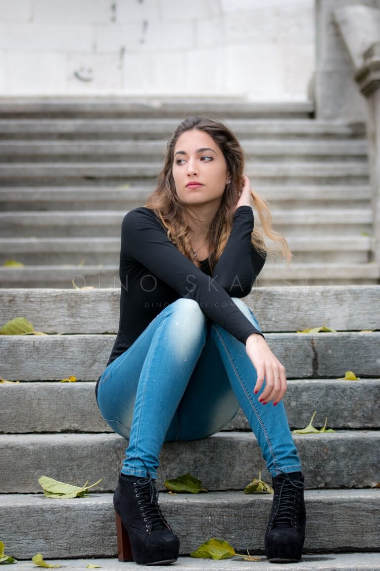 Colour portrait of a young woman in jeans sitting on stone steps