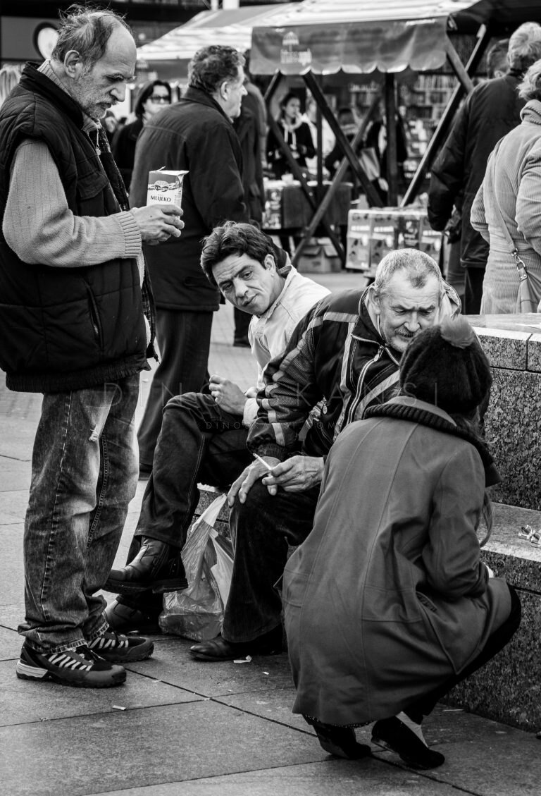 Black and white street photo of people sitting and talking on a pavement