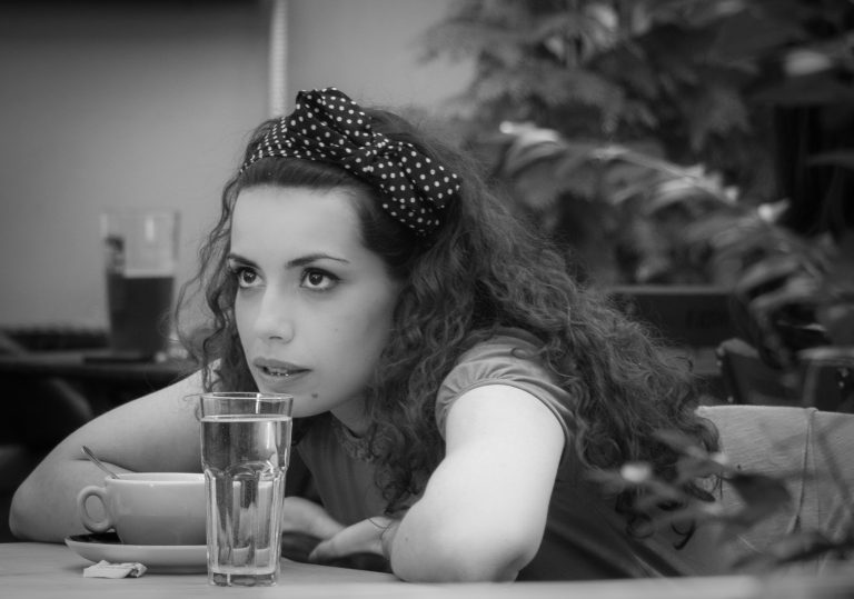Black and white portrait of a woman with a polka-dot headband sitting at a café table