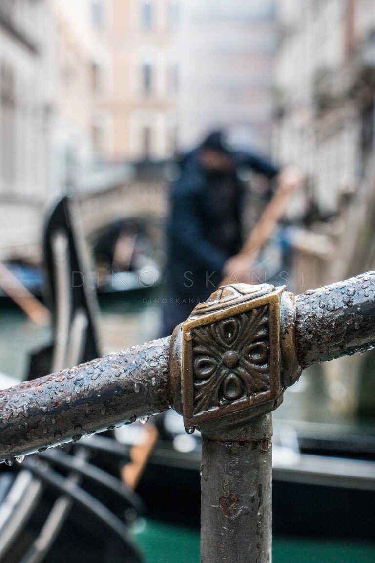 Close-up of an ornate metal railing with a gondolier blurred in the background, Venice