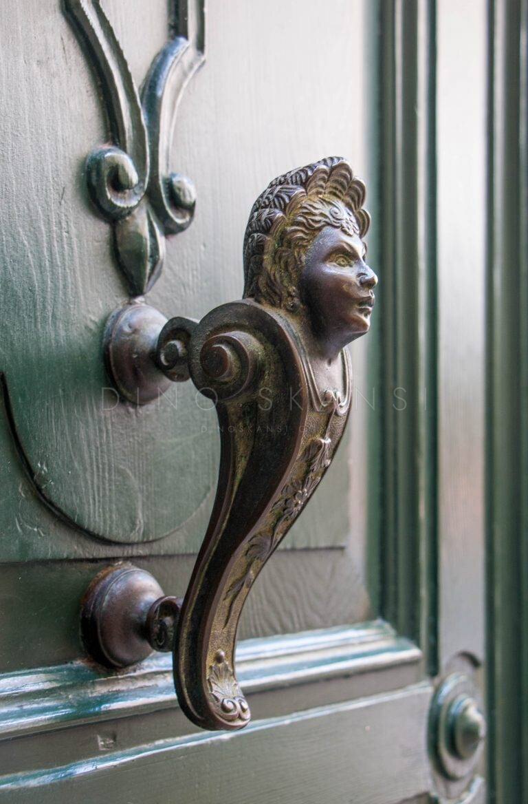 Brass door handle shaped like a figure's head on a green door in Venice