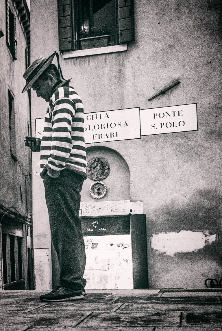 Black and white photo of a man in a striped shirt and straw hat on a Venice street corner